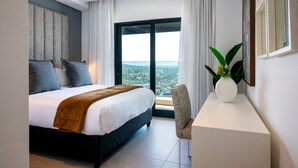 Une chambre d’hôtel avec un lit, un bureau, une chaise, une grande fenêtre donnant sur la ville et une plante en pot.