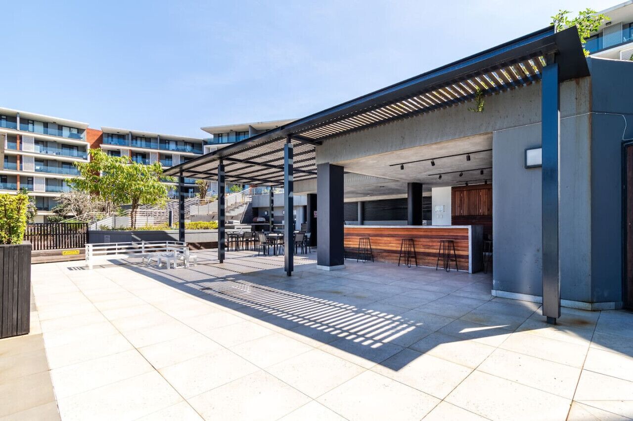 Et moderne udendørs opholdsområde med en overdækket terrasse, en bar samt en trappe til et højere niveau.