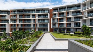 Un moderno edificio residenziale a più piani con balconi, un cortile centrale e un'area giardino curata.