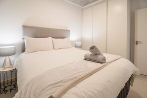 A neatly made bed with a white comforter and pillows, a folded towel on the bed, and a bedside lamp on a small table beside the bed. - Superb East 311 at Coral Point (Sibaya Precinct, KwaZulu-Natal)