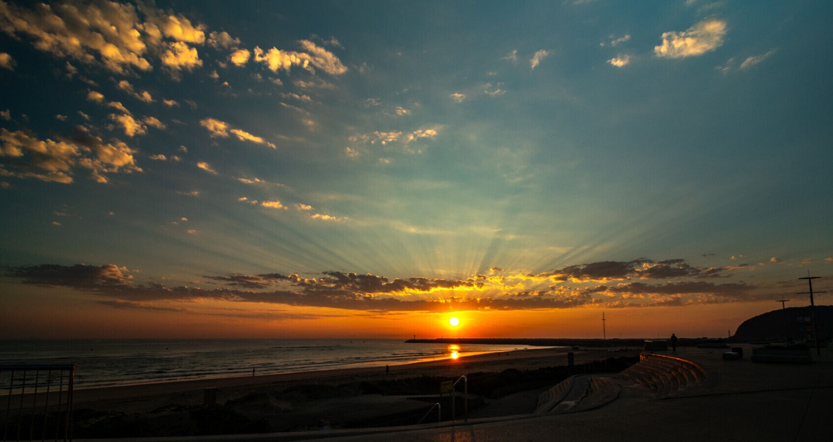 Un coucher de soleil sur une plage, avec une jetée qui s’avance dans l’eau.