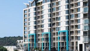 Un edificio residencial de varios pisos con balcones, una piscina delantera y un cielo despejado.