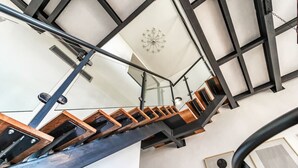 Una escalera moderna con escalones de madera y barandillas metálicas que conduce a un techo blanco con un candelabro.