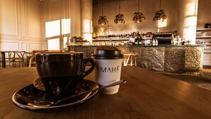 Interior de una cafetería con barra, mesas de madera y una taza de café sobre un platillo.