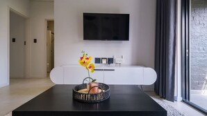 A modern living room with a black coffee table, a white cabinet, and a flat-screen TV mounted on the wall.