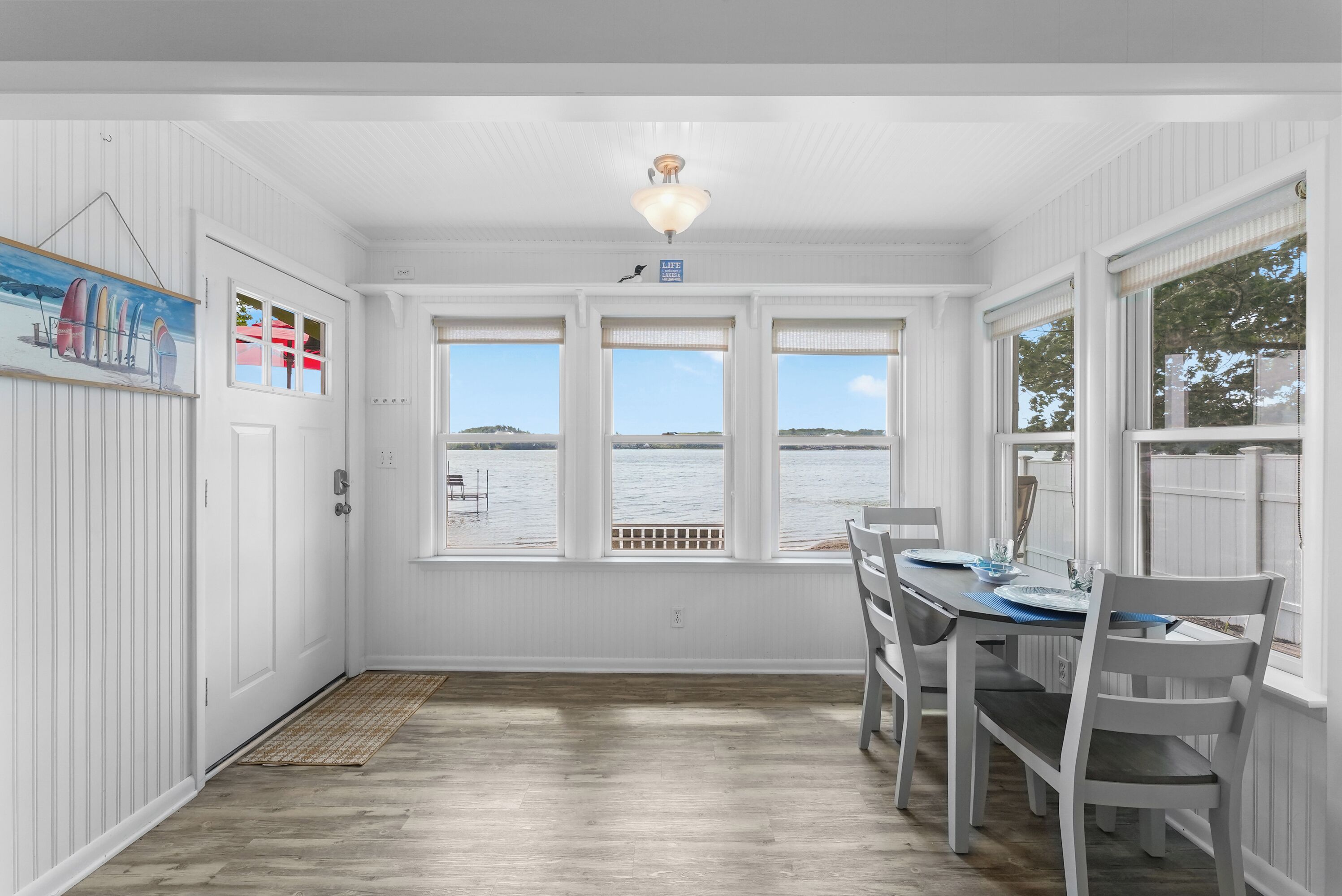 A dining area with a view of the water, white walls, and a ceiling light.