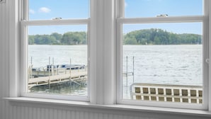 A view through a window of a docked boat, a clear sky, and a forested shoreline.