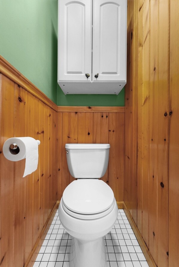 Un baño con paneles de madera, un inodoro blanco y un rollo de papel higiénico en la pared.