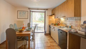 A kitchen with wooden cabinets, a dining area with chairs and a table, and a view through a glass door to an outdoor area. - Ca Cornocc With Private Terrace in Gordola (Gordola)