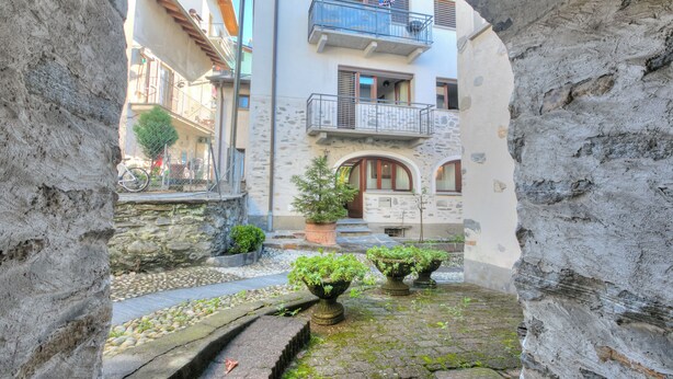 A stone archway leading to a courtyard with a building featuring a balcony and potted plants. - Ca Cornocc With Private Terrace in Gordola (Gordola)
