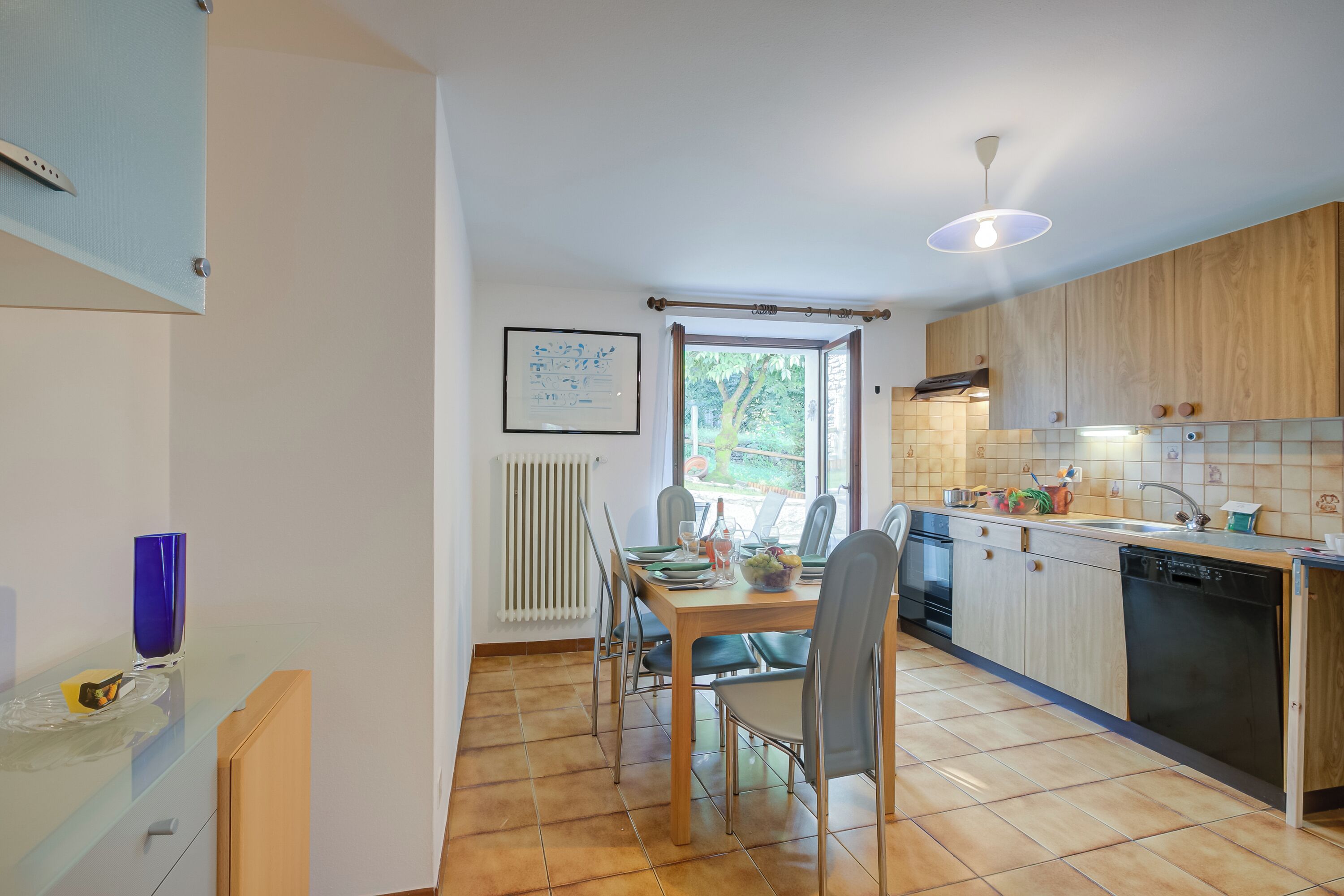 Een moderne keuken met houten kasten, een eettafel met stoelen, een raam met gordijnen en een radiator.