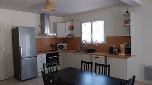 A modern kitchen with a refrigerator, microwave, oven, sink, and dining area. - WELCOME VILLA (Andernos-les-Bains)