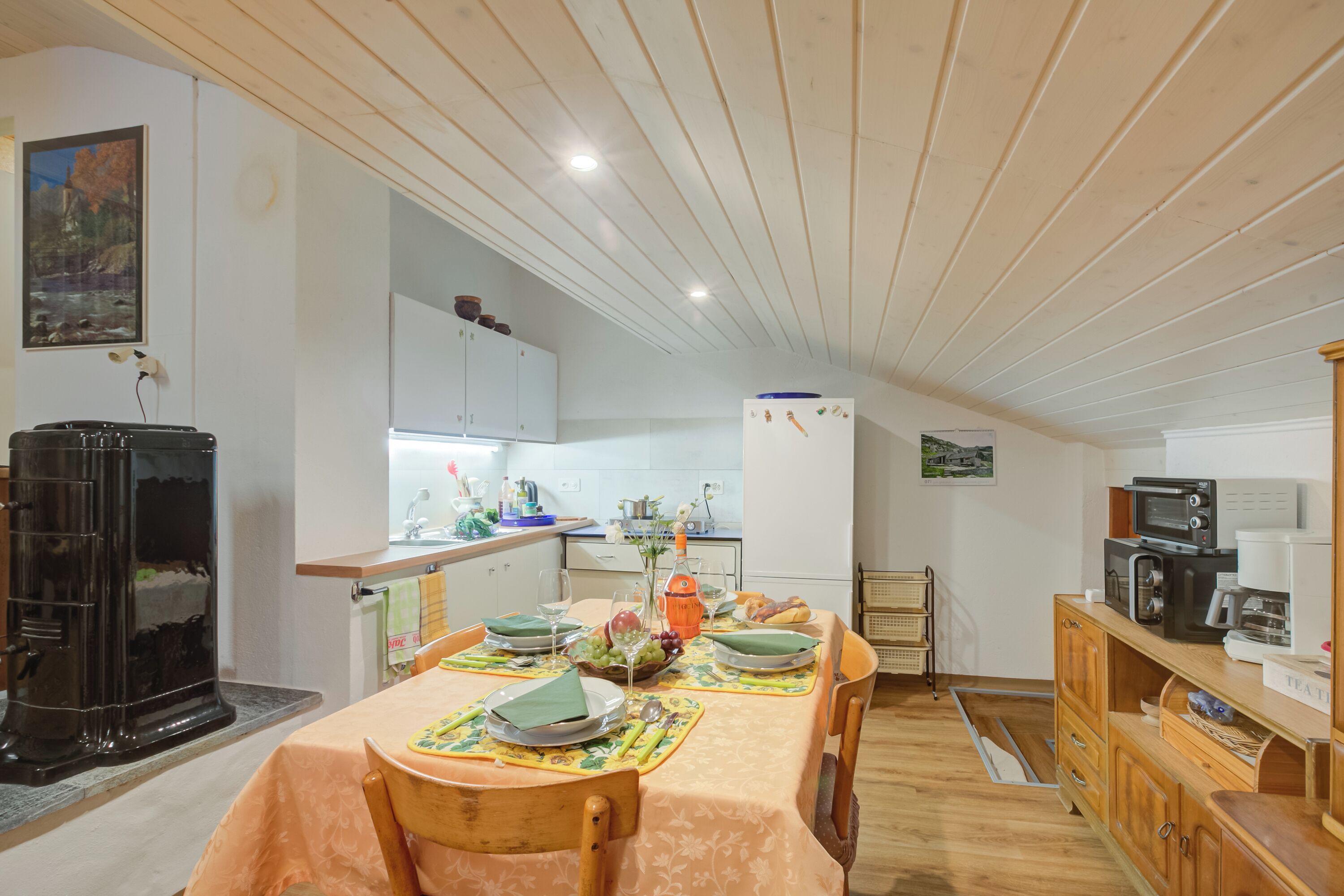 A dining area with a table set for four, a black stove, wooden cabinets, and a kitchen in the background.