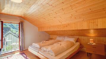 Ein Schlafzimmer einer Holzhütte mit zwei Betten, einem Nachttisch und Blick auf eine grüne Landschaft durch ein großes Fenster.