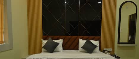 A hotel room with a large bed, a headboard with a geometric pattern, two wall-mounted light fixtures, a mirror, and a window with curtains.