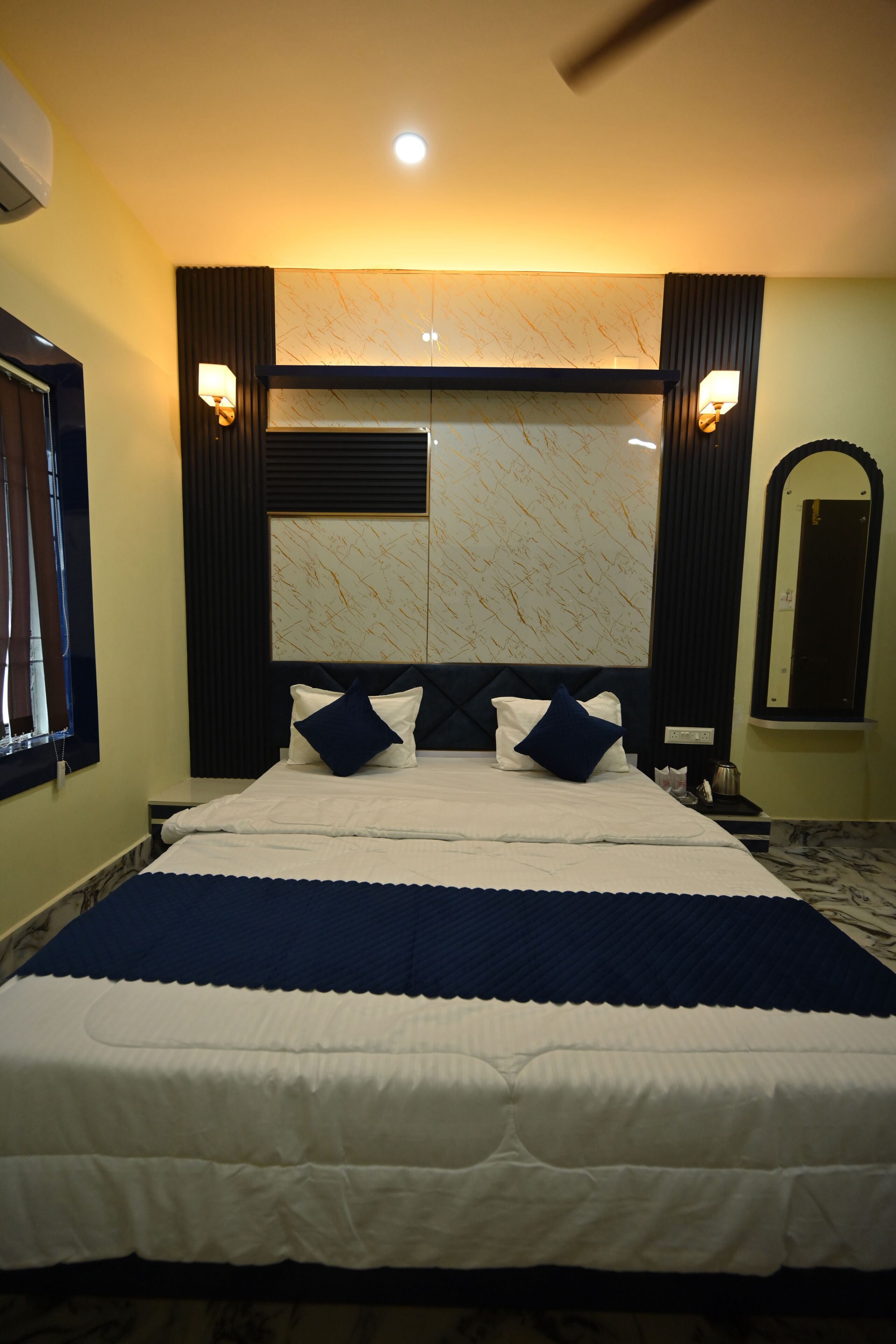A neatly made bed with a headboard, bedside tables, and a wall-mounted mirror.