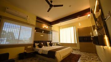 A bedroom with a bed, a ceiling fan, an air conditioning unit, a window with blinds, and a bathroom with a mirror and sink.