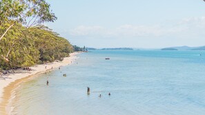 A beach with clear water, people swimming and sunbathing, and a boat in the distance. - Yawa at Yoolarai, 64 Yoolarai Cr - Ducted air, WiFi, Shared Pool (Nelson Bay)