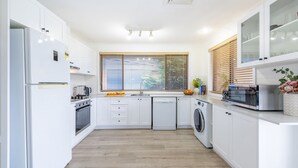 A modern kitchen with white cabinetry, a built-in oven, a dishwasher, a microwave, and a window with blinds. - Yawa at Yoolarai, 64 Yoolarai Cr - Ducted air, WiFi, Shared Pool (Nelson Bay)