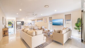 A spacious living area with a large sofa set, a dining table, and a kitchen in the background. - Shelly's Bay Escape, 27c Dowling St - stylish with ducted air con and Wi-Fi (Nelson Bay)