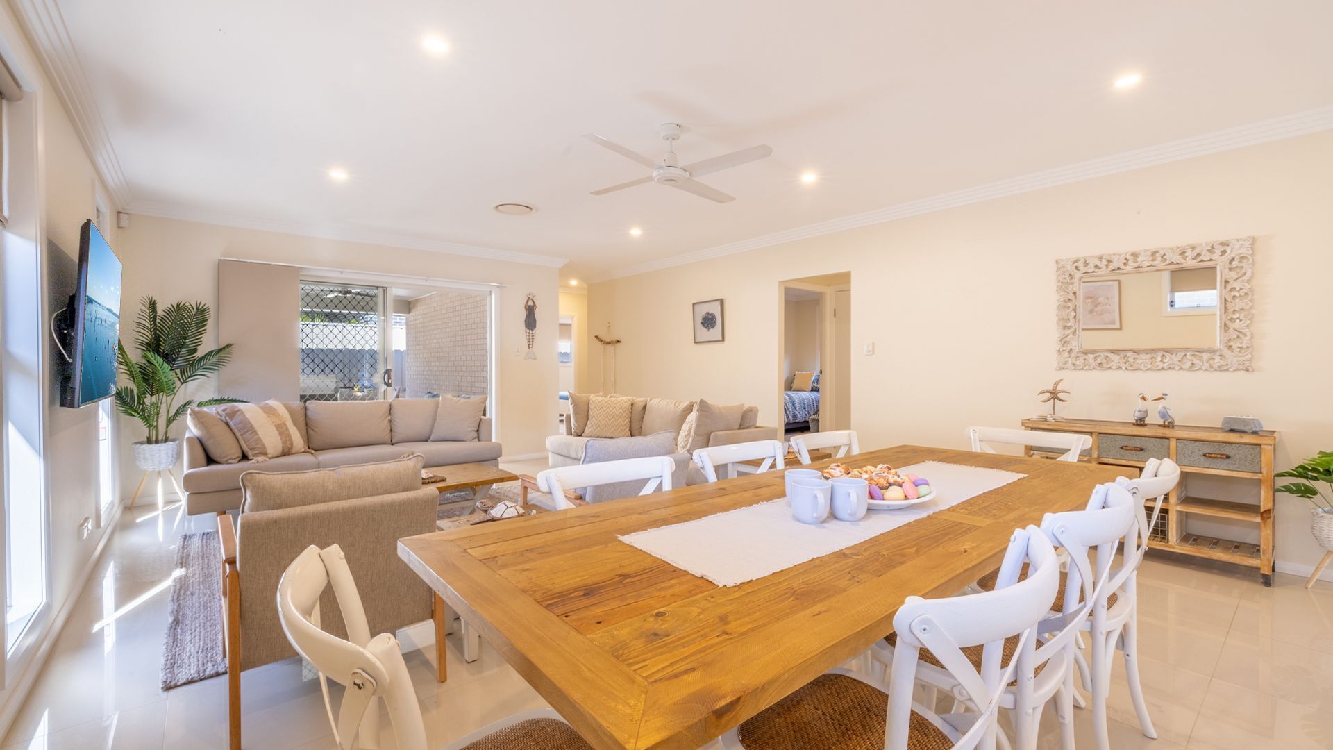 A spacious living area with a wooden dining table, white chairs, and a sofa.