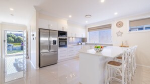 A modern kitchen with a stainless steel refrigerator, white cabinetry, and a large island with bar stools. - Shelly's Bay Escape, 27c Dowling St - stylish with ducted air con and Wi-Fi (Nelson Bay)