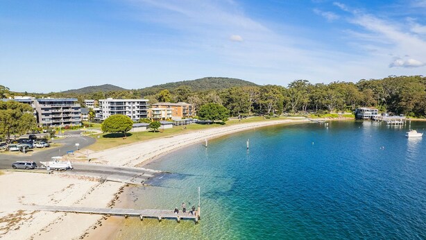 A coastal area with a sandy beach, a pier, and buildings in the background. - Shelly's Bay Escape, 27c Dowling St - stylish with ducted air con and Wi-Fi (Nelson Bay)