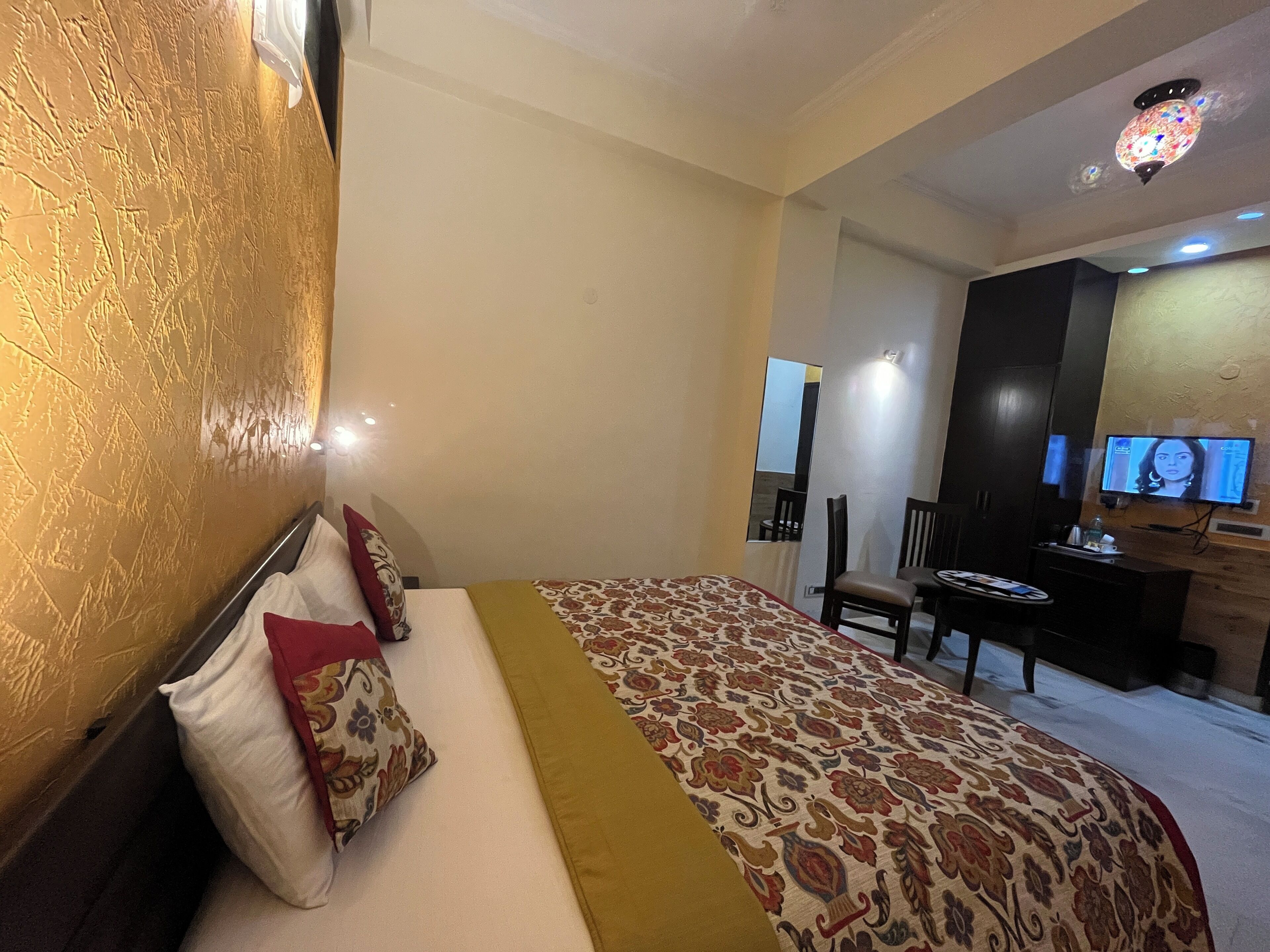 A hotel room with a large bed, a desk with a chair, a television, and a small table.