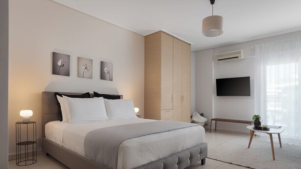 A modern bedroom with a large bed, bedside lamps, a TV, and a bench. - Athenian Comfort Apartments (Zografos)
