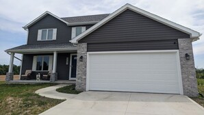 A two-story house with a dark exterior, a white garage door, and a covered porch with outdoor seating. - Charming 2-bedroom country house near South Bend and Potato Creek with WiFi, AC. (Bremen)