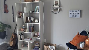 A living room with a white bookshelf, a guitar, a violin, a blue chair, and a rug. - Charming 2-bedroom country house near South Bend and Potato Creek with WiFi, AC. (Bremen)