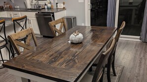 A dining room with a wooden table and chairs, a kitchen in the background, and a chandelier. - Charming 2-bedroom country house near South Bend and Potato Creek with WiFi, AC. (Bremen)