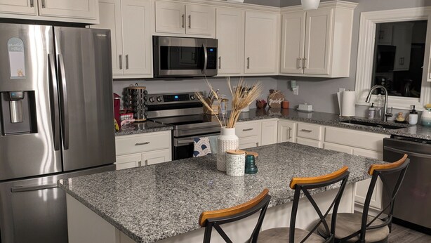 A modern kitchen with white cabinets, stainless steel appliances, granite countertops, and pendant lighting. - Charming 2-bedroom country house near South Bend and Potato Creek with WiFi, AC. (Bremen)