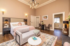 A bedroom with a large bed, bedside tables, a small round table, a sofa, and a patterned rug.