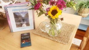 A wooden table with a glass vase of flowers, a book titled "Sea Salt Almond", and a framed picture on the table. - Cottage jewel -pet friendly (St. Augustine)