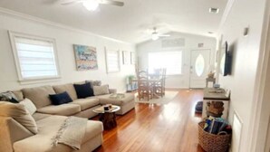 A spacious living room with a wooden floor, a sofa, a coffee table, and a dining area with chairs. - Cottage jewel -pet friendly (St. Augustine)