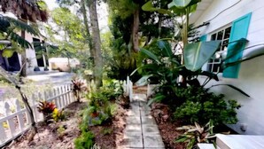 A narrow concrete pathway flanked by lush greenery and a white fence. - Cottage jewel -pet friendly (St. Augustine)