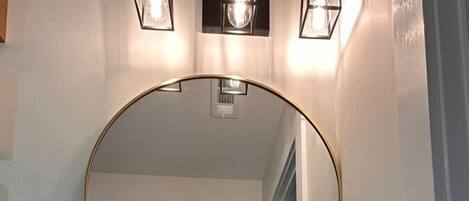 Une salle de bain avec un miroir rond, un lavabo blanc et trois lampes fixées au mur.