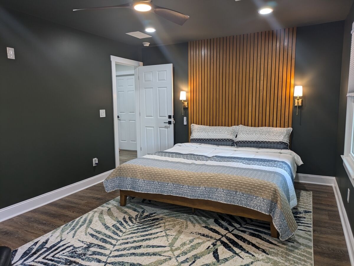 A bedroom with a bed, a wooden slat wall, a patterned rug, and a white door.