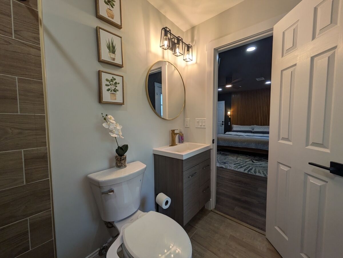A modern bathroom with a toilet, sink, and mirror. There are framed pictures on the wall and a small potted plant on the sink.