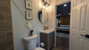 A modern bathroom with a toilet, sink, and mirror. There are framed pictures on the wall and a small potted plant on the sink.
