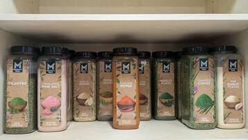 A shelf with various Member's Mark spice jars, including Cilantro, Himalayan Pink Salt, Minced Onion, Thyme Leaves, Cayenne Pepper, Parsley Flakes, Chopped Chives, and Fine Garlic Powder.