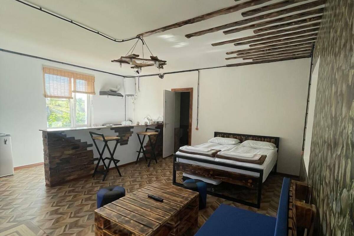 Quarto compacto com cama, pequeno espaço de cozinha e área de refeições.
