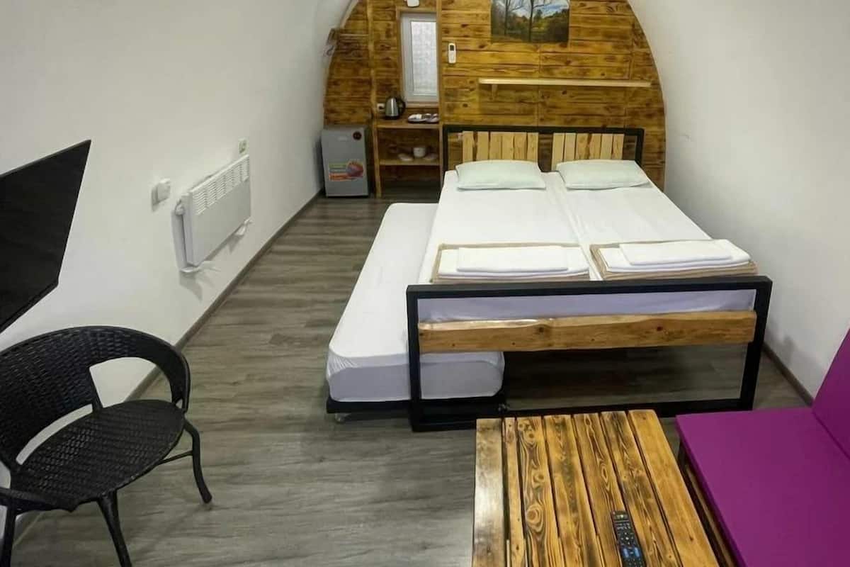 Um quarto pequeno e acolhedor com teto inclinado, uma cama, uma cadeira, uma mesa e um pequeno espaço com cozinha.