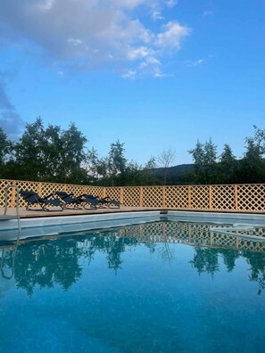 Una piscina cristalina con valla de madera y sillones de descanso.