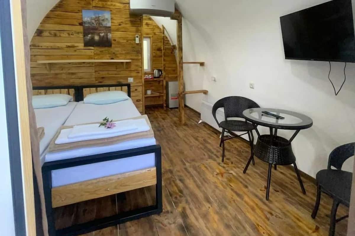 Quarto compacto com beliche, uma pequena mesa com cadeiras, televisão e teto de madeira.