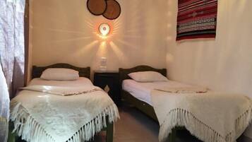 Quarto com duas camas, luminária pendente e um objeto decorativo na parede.
