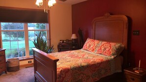 Une chambre à coucher comprenant un lit, une commode, une table de chevet et une fenêtre donnant sur un paysage verdoyant.