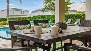 A dining table with chairs, a pool, and a view of houses in the background.
