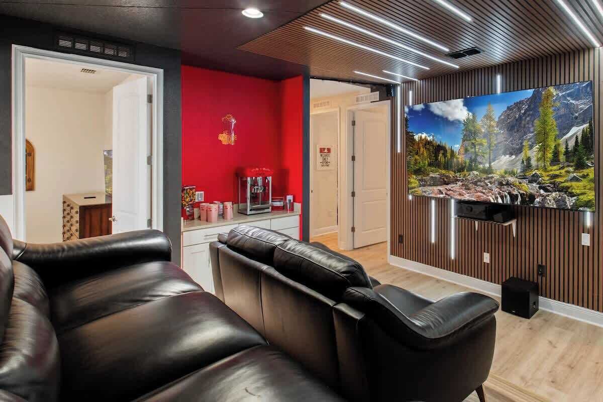 A modern living room with a red accent wall, a mounted TV, and a leather sofa.